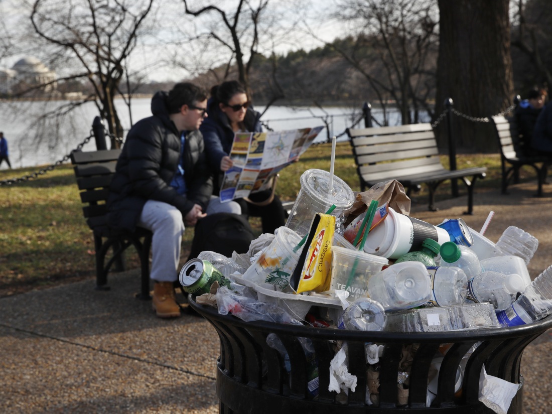 Uma lata de lixo transborda enquanto as pessoas sentam do lado de fora do Memorial Martin Luther King Jr. em Washington, DC