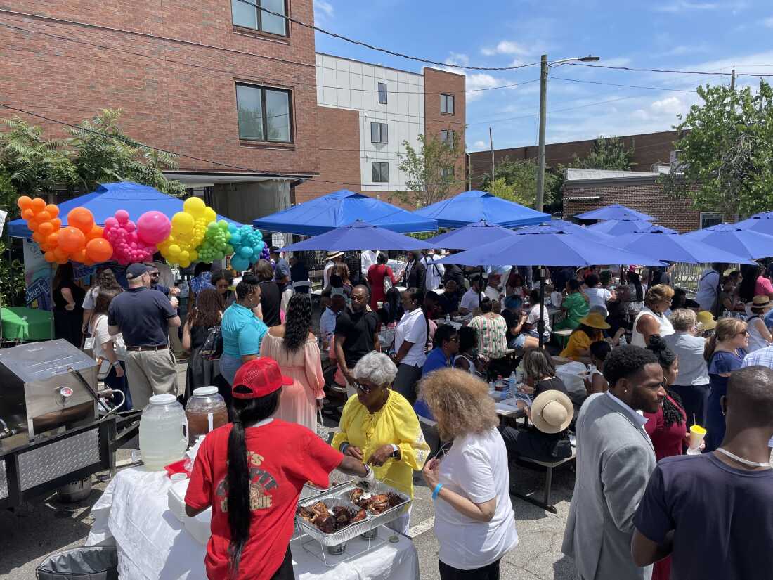 Pessoas comem ao ar livre sob guarda-sóis azuis em uma festa de quarteirão do Juneteenth para marcar a abertura do escritório da campanha de Biden em Atlanta.