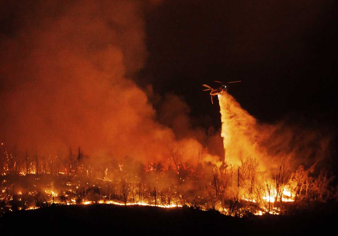 Um helicóptero voando à noite joga água nas chamas enquanto o incêndio Thompson queima na terça-feira em Oroville, Califórnia.